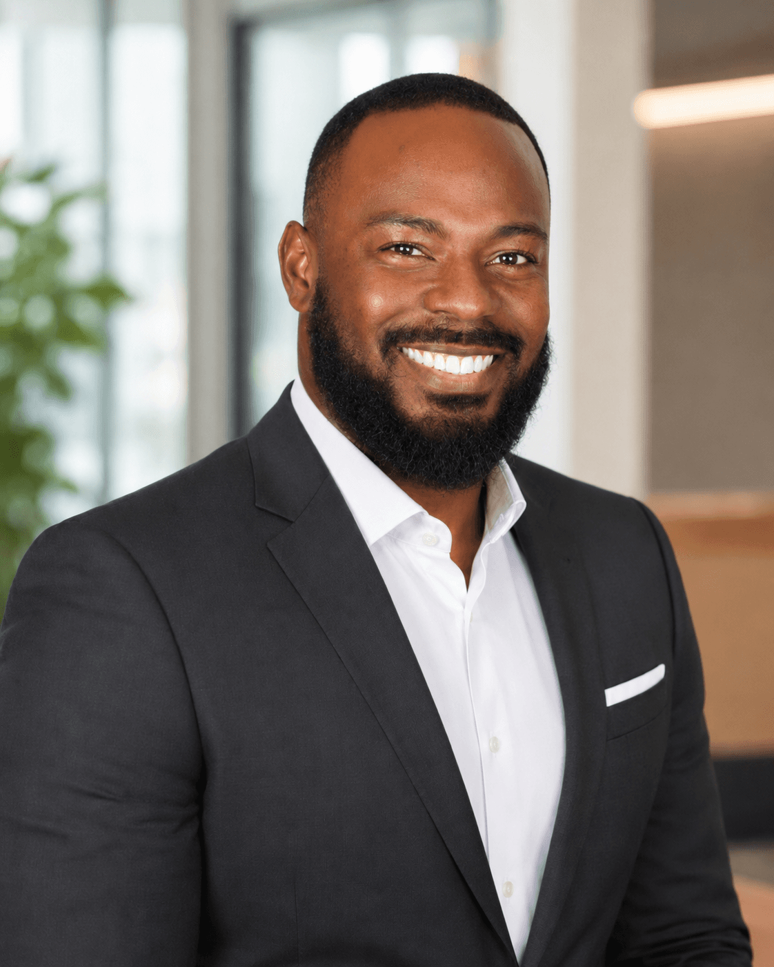 Smiling Black man with a beard wearing a dark suit jacket and white dress shirt.